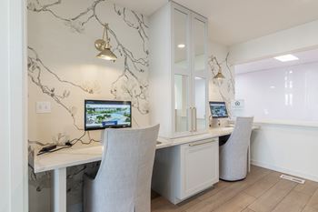 A white desk with a computer and chair in front of a cabinet with a wall hanging